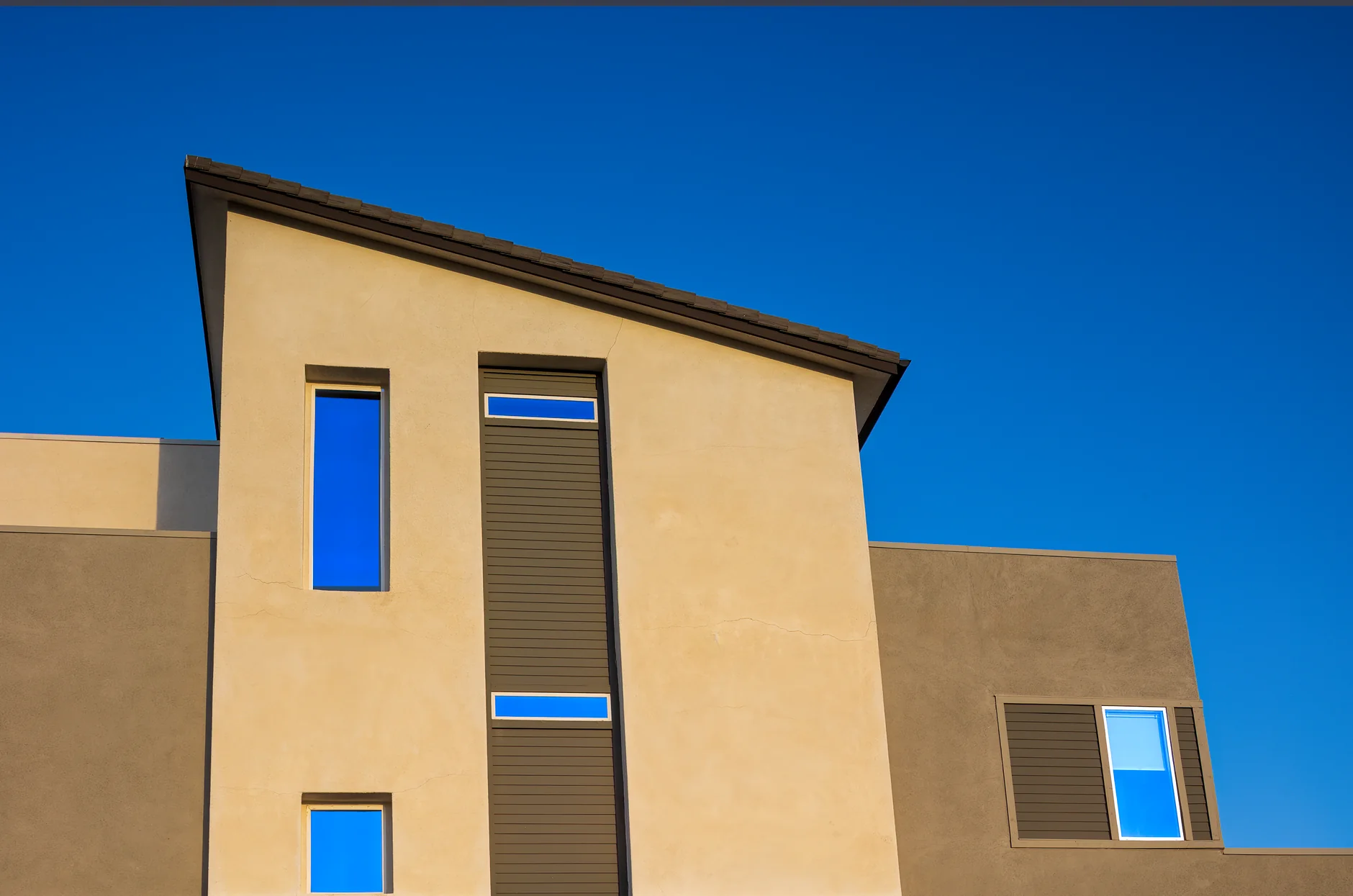 Modern residential building facade against a vivid blue sky, showcasing geometric windows.